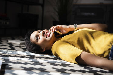 Young woman lying on the floor at home talking on the phone - GIOF07787