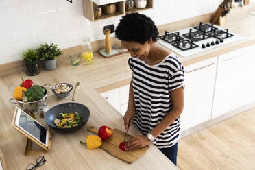 Junge Frau mit Tablet kochen in der Küche zu Hause Schneiden von Gemüse - GIOF07790