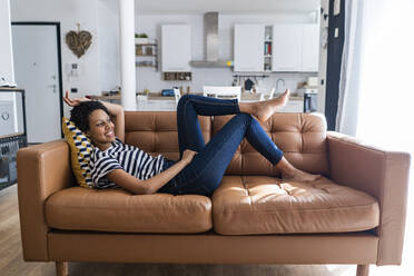 Entspannte junge Frau, die zu Hause auf der Couch liegt - GIOF07793