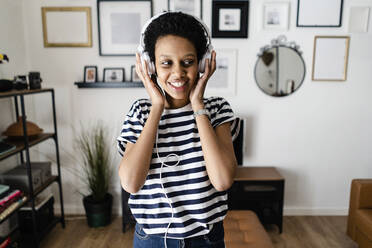 Glückliche junge Frau, die zu Hause mit Kopfhörern Musik hört - GIOF07802