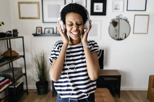 Glückliche junge Frau, die zu Hause mit Kopfhörern Musik hört - GIOF07803