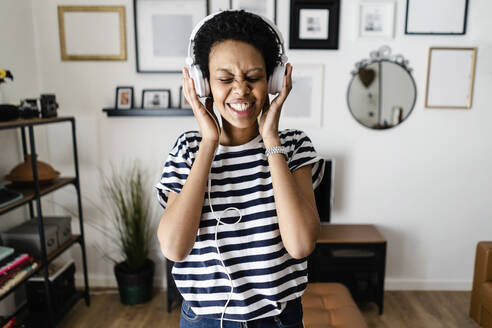 Happy young woman listening to music with headphones at home - GIOF07803