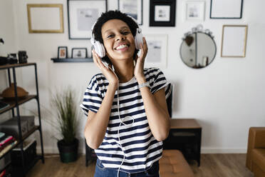 Happy young woman listening to music with headphones at home - GIOF07804