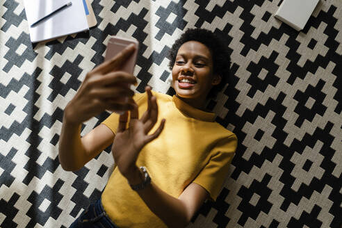 Young woman lying on carpet using smartphone - GIOF07826