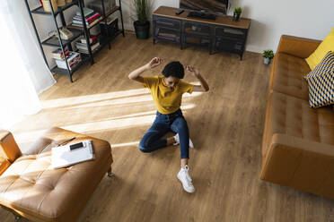 Excited young woman sitting on the floor at home - GIOF07829