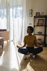 Junge Frau, die zu Hause auf dem Boden sitzt, in Yoga-Pose - GIOF07830