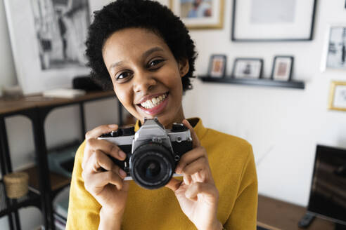 Porträt einer lächelnden jungen Frau mit einer alten Kamera zu Hause - GIOF07832
