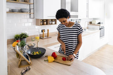 Junge Frau mit Tablet kochen in der Küche zu Hause Schneiden von Gemüse - GIOF07842