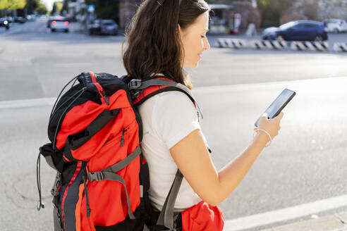 Junge Rucksackträgerin mit rotem Rucksack und Smartphone in der Stadt, Verona, Italien - GIOF07869