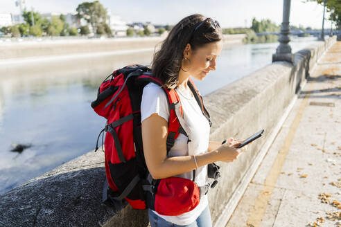 Junge Rucksacktouristin mit Smartphone an einem Fluss in Verona, Italien - GIOF07871