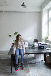 Girl with roller skates sitting on desk in office - GUSF02693