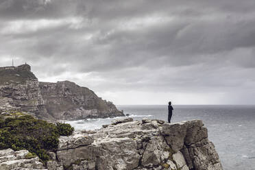 Mann steht auf einer felsigen Klippe und schaut auf den Horizont, Cape Point, Westkap, Südafrika - MCF00327