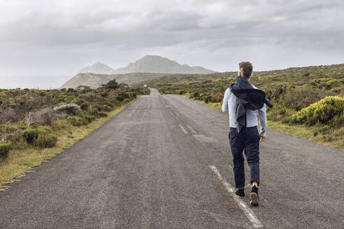 Rückenansicht eines Geschäftsmannes, der auf einer Landstraße spazieren geht, Cape Point, Westkap, Südafrika - MCF00336