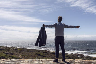 Rückenansicht eines Geschäftsmannes, der vor dem Meer steht, Cape Point, Westkap, Südafrika - MCF00339