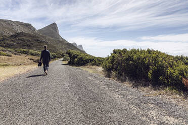 Back view of businessman walking barefoot on country road, Cape Point, Western Cape, South Africa - MCF00350
