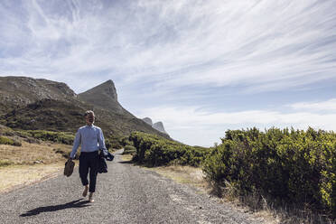 Businessman walking barefoot on country road, Cape Point, Western Cape, South Africa - MCF00351