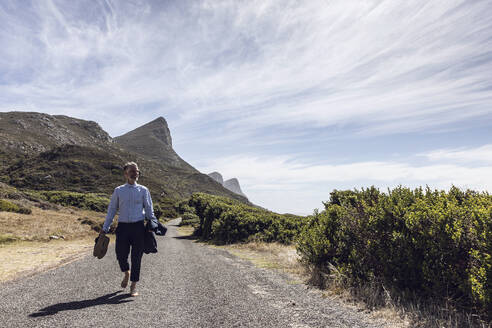 Geschäftsmann, der barfuß auf einer Landstraße läuft, Cape Point, Westkap, Südafrika - MCF00351