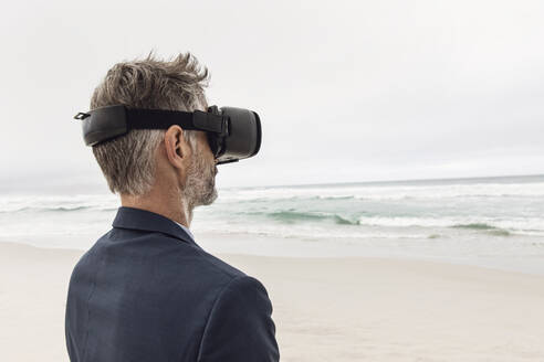 Geschäftsmann mit VR-Brille am Strand, Nordhoek, Westkap, Südafrika - MCF00354