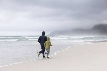 Rückenansicht von Vater und Tochter beim Joggen am Strand, Nordhoek, Westkap, Südafrika - MCF00357