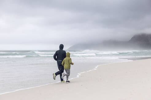 Rückenansicht von Vater und Tochter beim Joggen am Strand, Nordhoek, Westkap, Südafrika - MCF00357