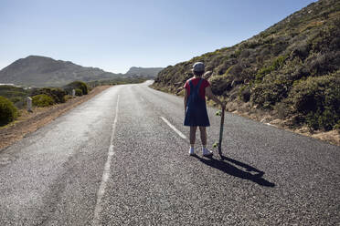 Back view of girl with skateboard standing on country road, Cape Town, Western Cape, South Africa - MCF00373