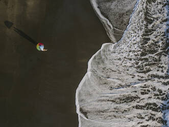 Luftaufnahme von Paar unter Regenbogenfarben Regenschirm am Strand, Kedungu Strand, Bali, Indonesien - KNTF03730