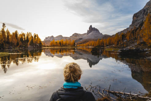 Female hiker looking at the mountain landscape with lake at the first light of the day, Dolomites Alps, Cortina, Italy - MRAF00440