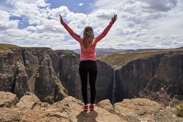 Frau mit hochgestreckten Armen, die die Landschaft an den Maletsunyane-Wasserfällen in Lesotho genießt - VEGF00845