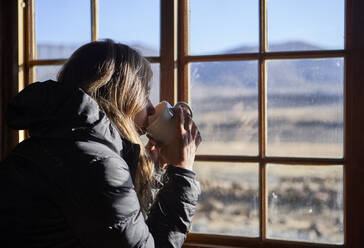 Frau trinkt eine Tasse Kaffee und bewundert die Berge durch das Fenster - VEGF00852