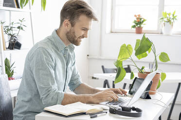 Smiling man using laptop at desk in office - VPIF01754