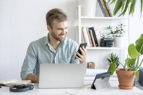 Lächelnder Mann mit Smartphone am Schreibtisch im Büro, lizenzfreies Stockfoto