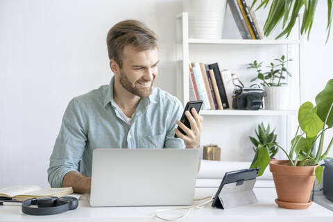 Smiling man using smartphone at desk in office stock photo