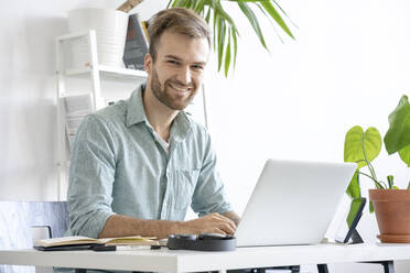 Porträt eines lächelnden Mannes mit Laptop am Schreibtisch im Büro - VPIF01757