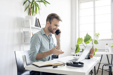 Lächelnder Mann am Telefon am Schreibtisch im Büro - VPIF01759