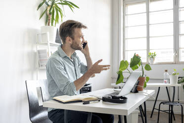 Lächelnder Mann am Telefon am Schreibtisch im Büro - VPIF01760