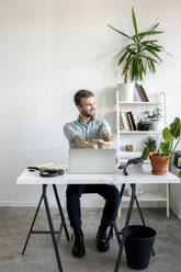 Lächelnder Mann am Schreibtisch im Büro mit Blick zur Seite - VPIF01761