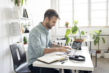 Lächelnder Mann mit Laptop am Schreibtisch im Büro - VPIF01763