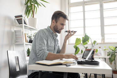 Mann mit Smartphone und Laptop am Schreibtisch im Büro - VPIF01768