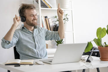 Aufgeregter Mann beim Musikhören am Schreibtisch im Büro - VPIF01776