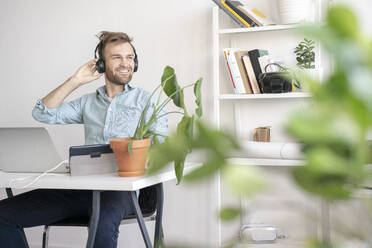 Smiling man listening to music at desk in office - VPIF01777