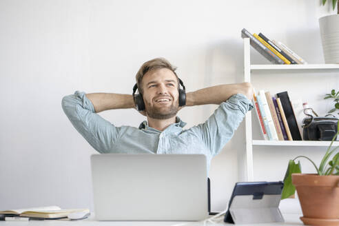 Lächelnder Mann beim Musikhören am Schreibtisch im Büro - VPIF01778