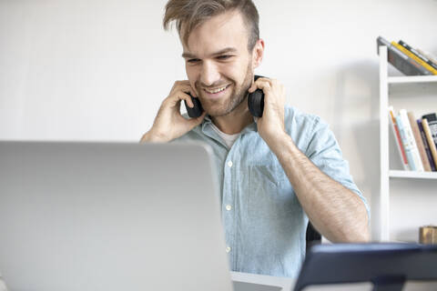 Smiling man with headphones and laptop at desk in office stock photo