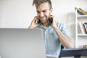 Lächelnder Mann mit Kopfhörern und Laptop am Schreibtisch im Büro - VPIF01781