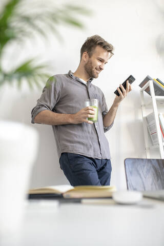 Lächelnder Mann mit Smartphone im Büro, lizenzfreies Stockfoto