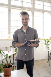 Porträt eines lächelnden Mannes mit einem Buch in einem Büro - VPIF01791