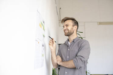 Lächelnder Mann, der an der Wand im Büro an einem Papier arbeitet - VPIF01796