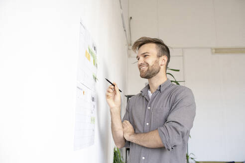 Smiling man working on paper at the wall in office - VPIF01796