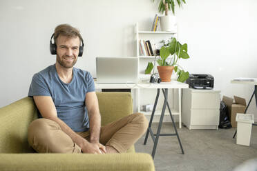 Porträt eines lächelnden Mannes, der auf einer Couch im Büro sitzt und Musik hört - VPIF01819