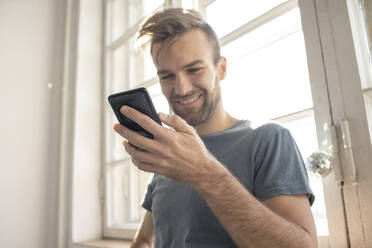 Lächelnder Mann mit Smartphone am Fenster - VPIF01824