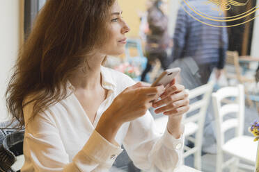 Portrait of young woman holding cell phone in a cafe - FMOF00757